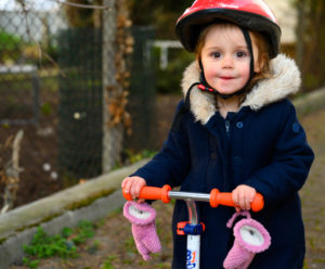 Petite fille avec un casque rouge qui fait de la trottinette, photographe enfants lifestyle Houilles
