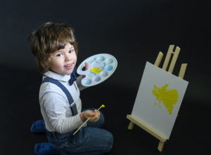 Petit garçon sur fond noir en train de peindre sur un petit chevalet Photographe enfant Houilles Photographe enfants Houilles Photographe Houilles