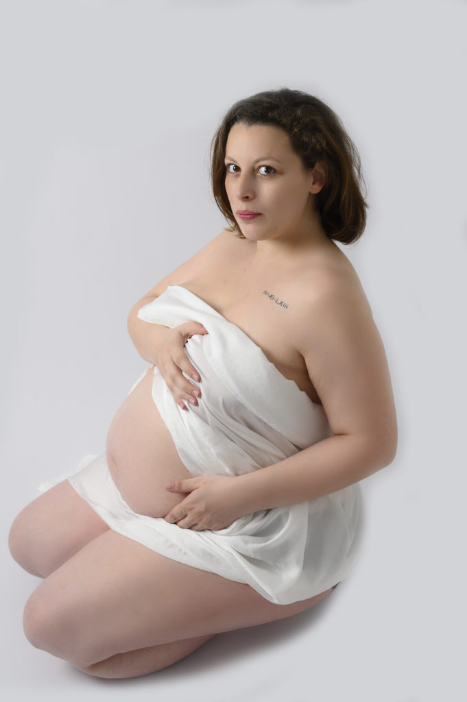 femme enceinte assise sur ses genoux poitrine couverte par un voile en soie blanc photographe grossesse Houilles photographe maternité Houilles photographe femme enceinte Houilles photographe Houilles