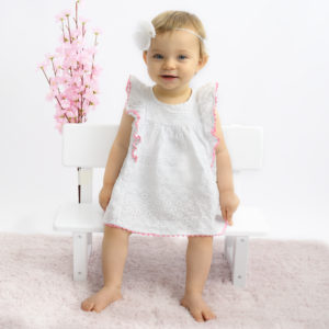 Bébé de 10 mois assise sur un petit banc, robe blanche bandeau blanc fleurs et tapis roses Photographe bébé Houilles photographe Houilles