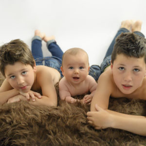 bébé et ses deux grands frères à plat ventre sur un tapis de fausse fourrure marron photographe enfant Houilles photographe bébé Houilles photographe famille Houilles photographe enfant photographe bébé photographe famille