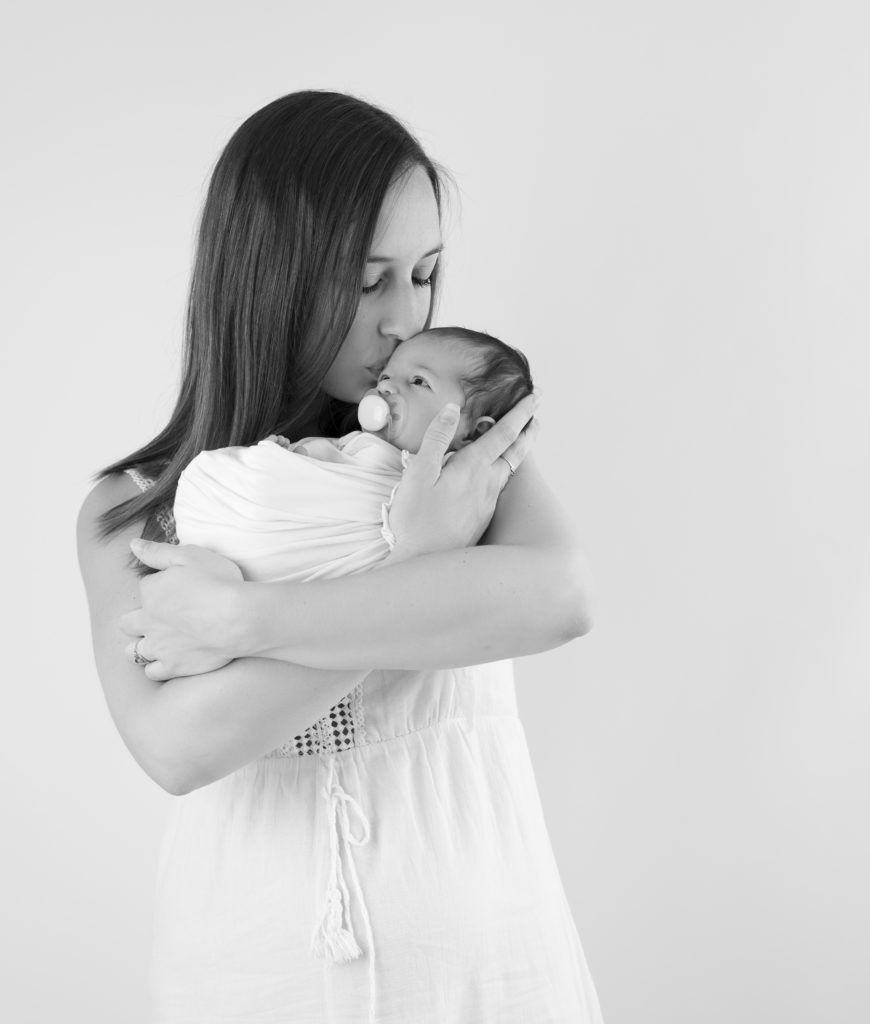 Portrait noir et blanc d'une jeune maman qui embrasse sa toute petite fille emmaillotée de blanc
photographe naissance Houilles Yvelines photographe nouveau-né Houilles Yvelines