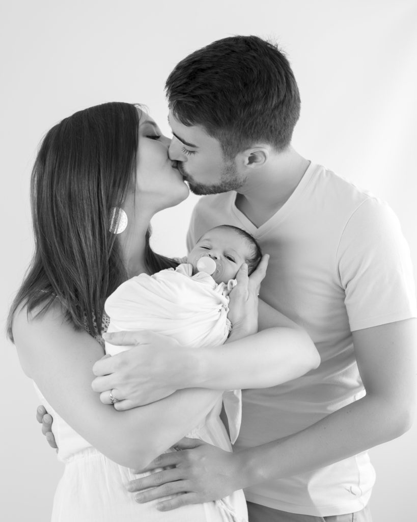 Jeunes parents qui s'embrassent en tenant leur nouveau-né dans les bras photographe famille Houilles Yvelines