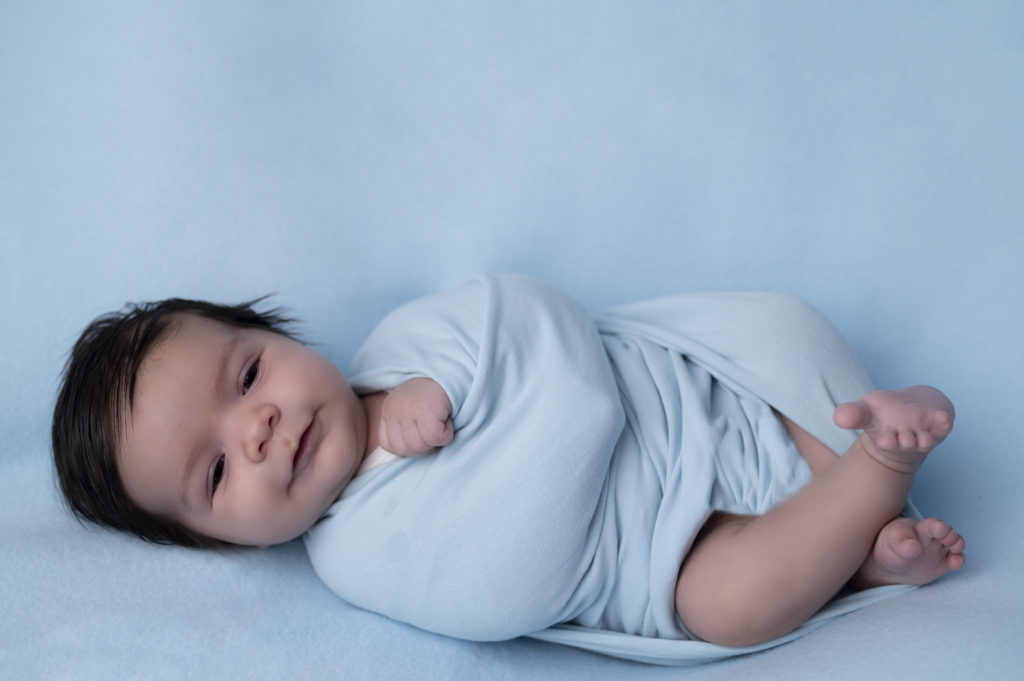 Nouveau-né sur beanbag emmailloté de bleu qui sourit
photographe naissance nouveau-né Houilles Yvelines