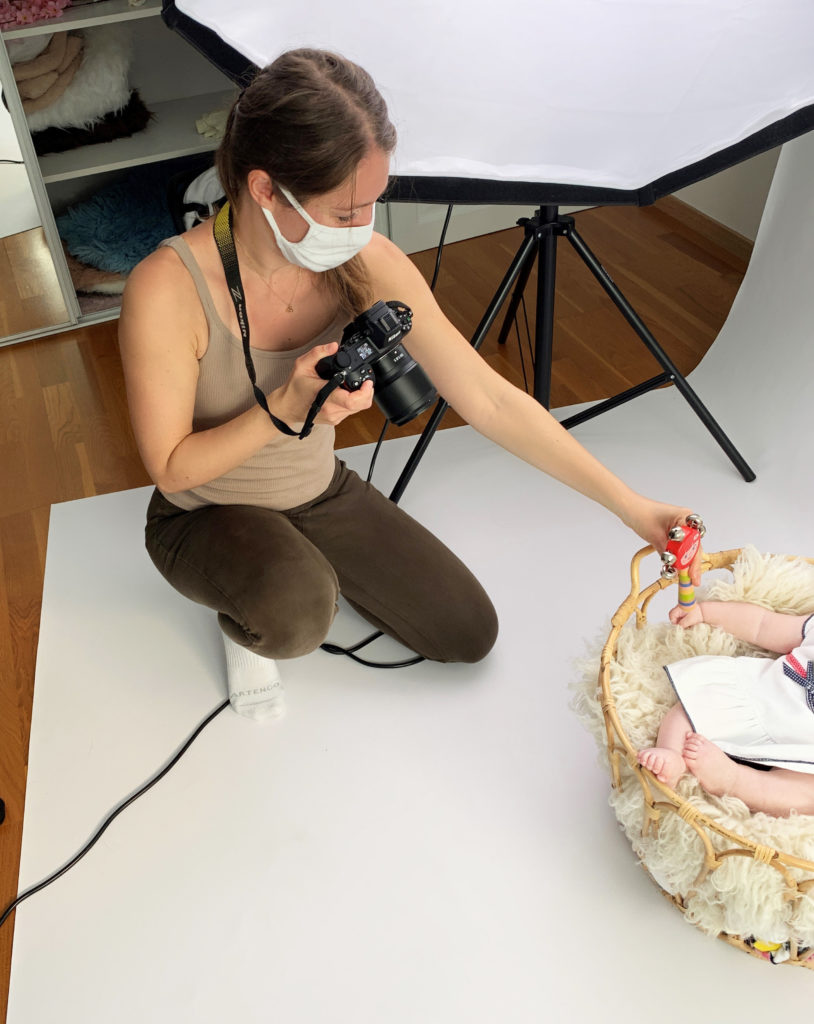 photographe en train de donner un hochet à bébé assise dans un panier garni de blanc 
photographe bébé Houilles la Défense Yvelines