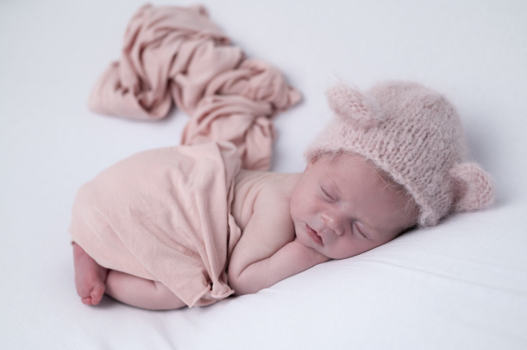 nouveau-né wrap et bonnet roses endormi en pose bump up sur beanbag photographe naissance nouveau-né houilles yvelines la défense