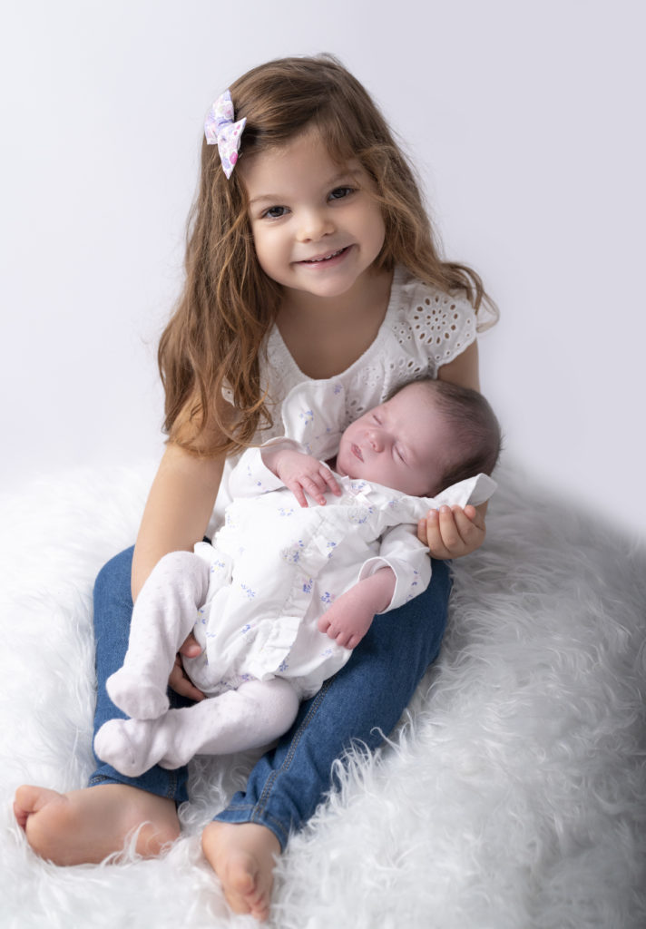petite fille de trois ans qui tient sa petite soeur nouvelle-née dans ses bras photographe naissance nouveau-né Houilles Yvelines la Défense