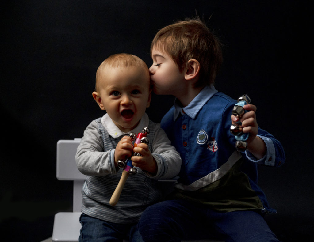 deux frères assis côte à côte le grand frère fait un bisou à son petit frère qui fait un grand sourire photographe bébé famille Houilles Yvelines la Défense