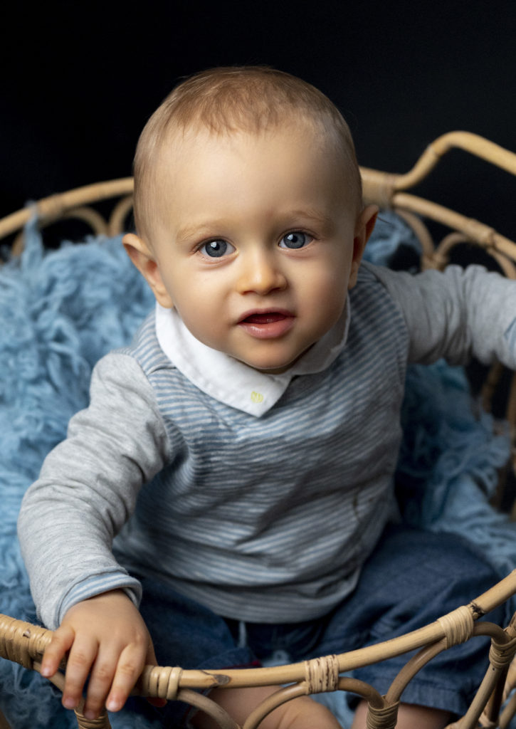portrait d'un bébé d'un an qui sourit assis sur un petit banc blanc. Photographe bébé enfant famille Houilles Yvelines la Défense