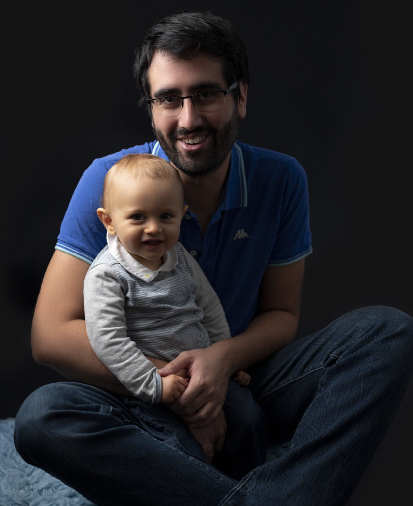 bébé de un an qui sourit sur les genoux de son papa photographe bébé famille Houilles Yvelines la Défense