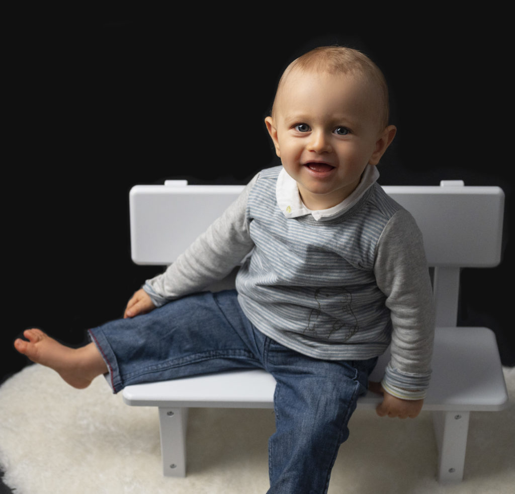 portrait d'un bébé de un an qui sourit assis sur un petit banc blanc. Photographe bébé enfant famille Houilles