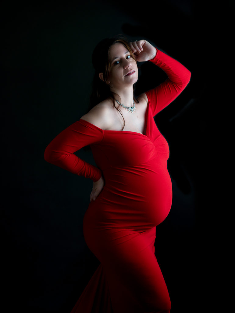 Femme enceinte vêtue d'une robe de créatrice rouge sur fond noir photographe grossesse maternité Houilles Yvelines la défense