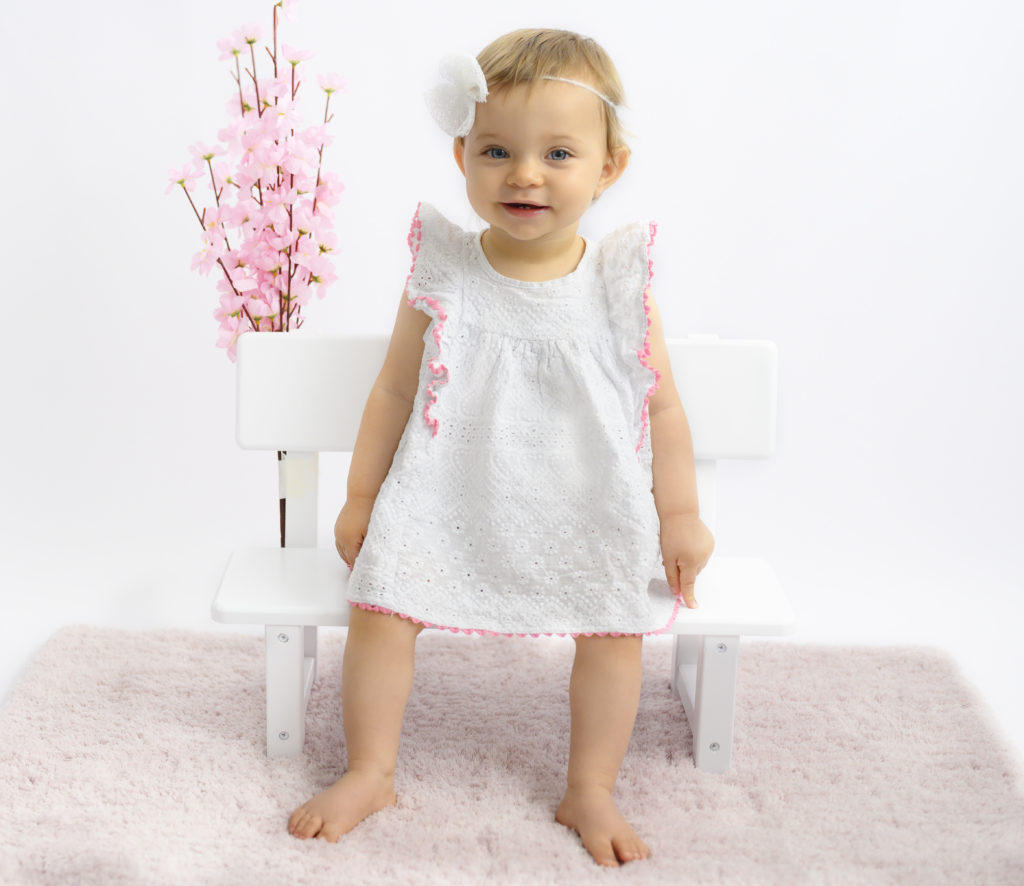 bébé fille de 12 mois assise sur un banc fleuri sourit photographe bébé Houilles Yvelines la Défense