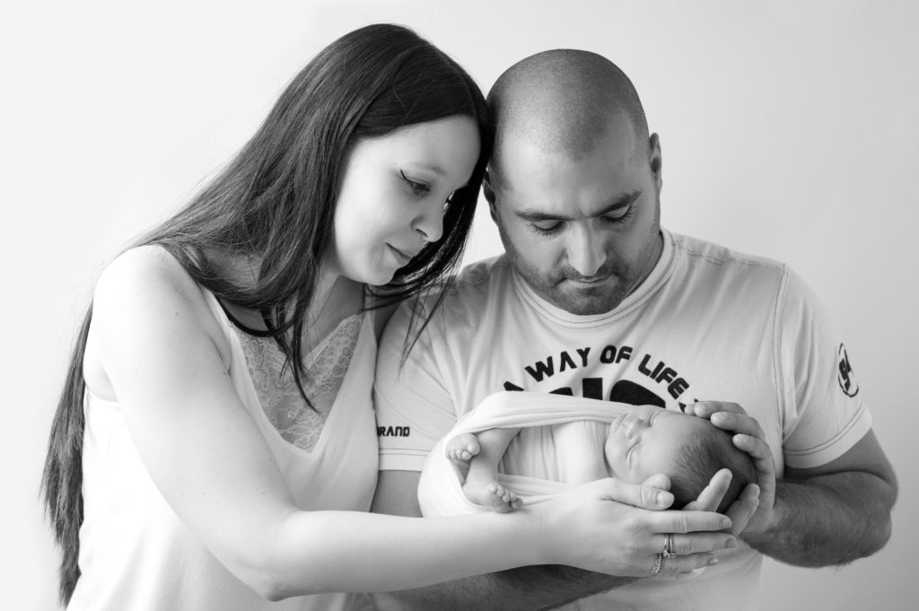 portrait noir et blanc d'une famille tenant un nouveau-né dans ses mains photographe naissance nouveau né Houilles Yvelines la Défense