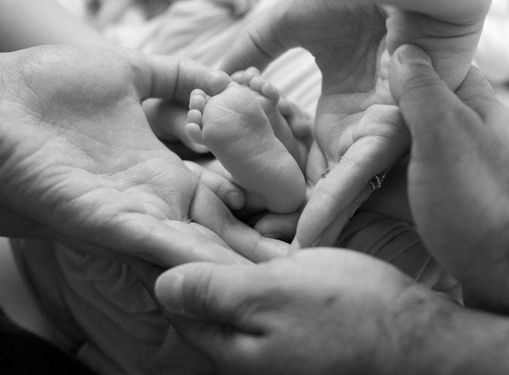 tout-petits pieds tenus par la grande soeur, le papa et la maman de bébé. Photographe naissance nouveau-né famille Houilles Yvelines la Défense