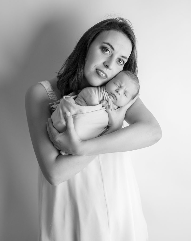 portrait noir et blanc d'une jeune maman tenant son bébé emmailloté endormi dans ses bras photographe naissance nouveau-né bébé Houilles Yvelines la Défense