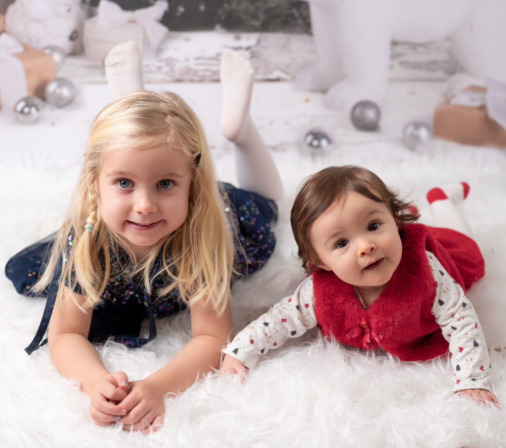 Petites filles de 4 anas et 6 mois allongées côte à côte à plat ventre dans un décor de Noël photographe bébé enfant famille Houilles Yvelines la Défense