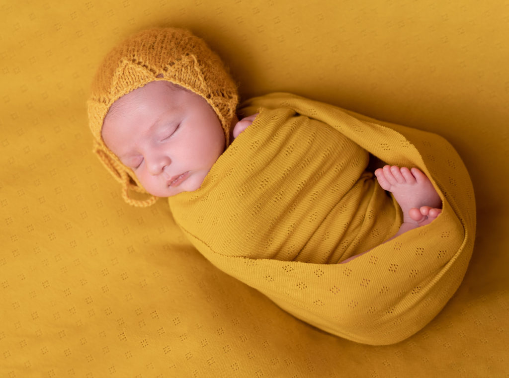 nouveau-né emmailloté de jaune béguin jaune moutarde sur posing bag jaune moutarde photographe naissance nouveau-né Houilles Yvelines la Défense