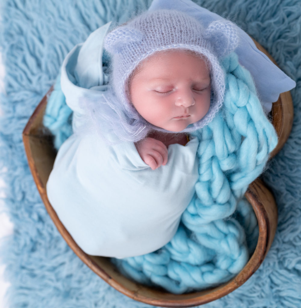 nouveau-né emmailloté de bleu avec un bonnet d'ours bleu endormi dans coeur en bois sur tresse en laine bleue photographe naissance nouveau-né Houilles Yvelines la Défense