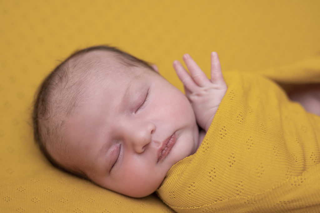 gros plan sur le visage et la petite main d'un nouveau-né endormi sur posing bag jaune moutarde photographe naissance nouveau-né Houilles Yvelines la Défense