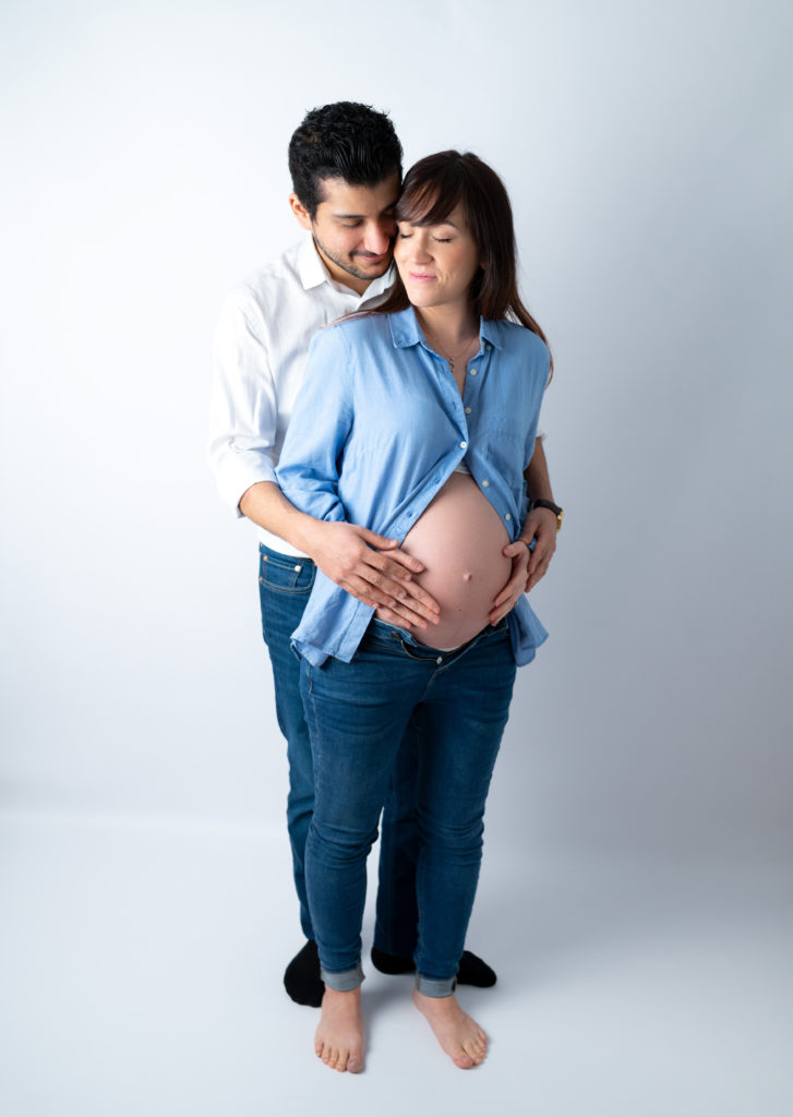 couple en jean et chemise mains sur le ventre de la femme enceinte photographe grossesse maternité Houilles Yvelines la Défense