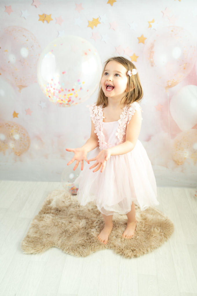 Petite fille sur fond ballons et étoiles joue avec un ballon confettis photographe enfant anniversaire Houilles Yvelines la Défense