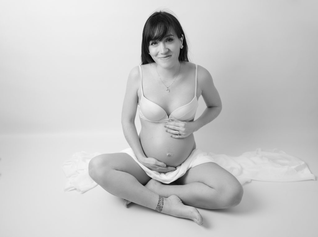 portrait noir et blanc d'une femme enceinte assise en tailleur avec un voile de soie blanche sur les genoux photographe grossesse maternité Houilles Yvelines la Défense