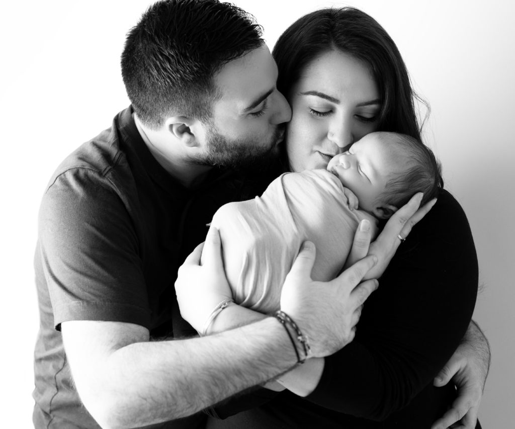 portrait noir et blanc de jeunes parents tenant leur nouveau-né emmailloté dans leurs bras photographe naissance famille Houilles Yvelines la Défense