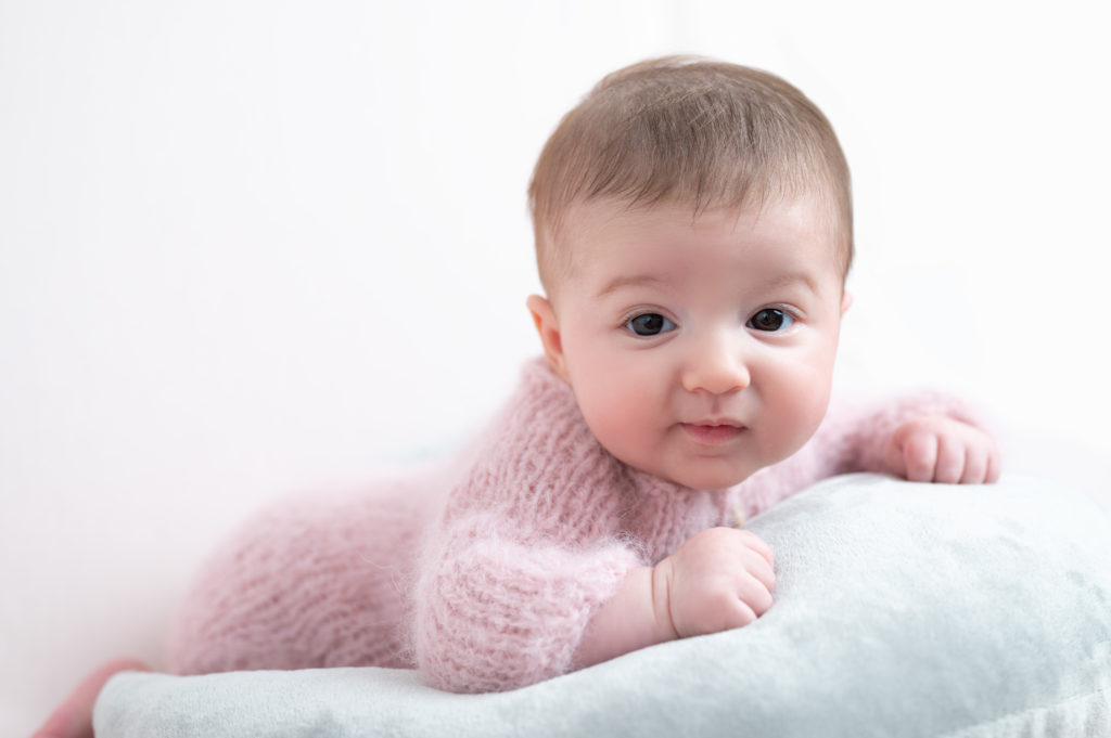 bébé de deux mois en body laine doudou rose pâle allongée sur le ventre sur une lune grise sur fond rose photographe bébé Houilles Yvelines la Défense