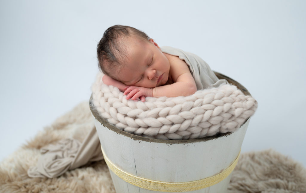 nouveau-né endormi dans un seau en bois le menton sur les mains photographe naissance nouveau-né Houilles Yvelines la Défense