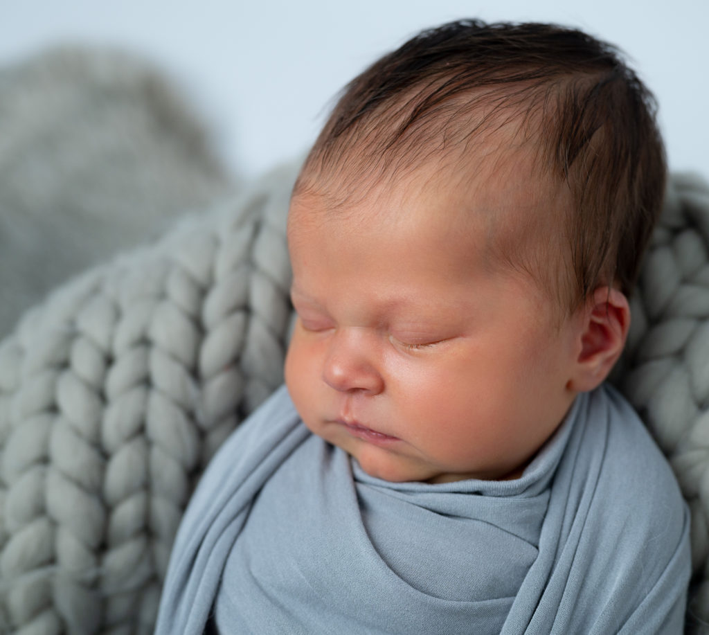 nouveau-né emmailloté de gris endormi dans un panier rond sur pose bébé gris. Photographe naissance nouveau-né Houilles Yvelines la Défense