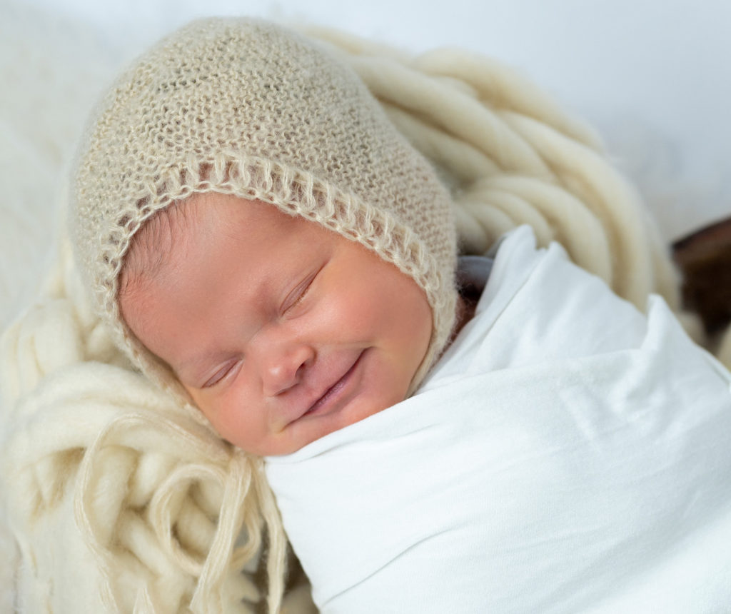 nouveau-né endormi dans coeur en bois sur tresse en laine écrue bonnet beige sourit photographe naissance nouveau-né Houilles Yvelines la Défense