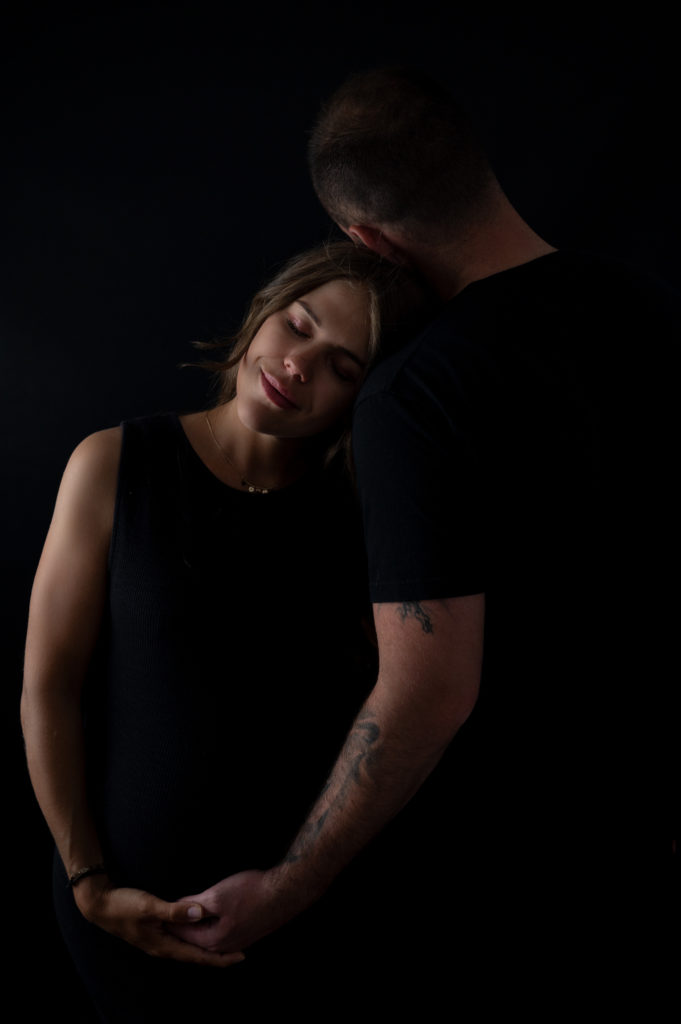 portrait noir et blanc d'un jeune couple de futurs parents sur fond noir photographe grossesse femme enceinte maternité Houilles Yvelines la Défense