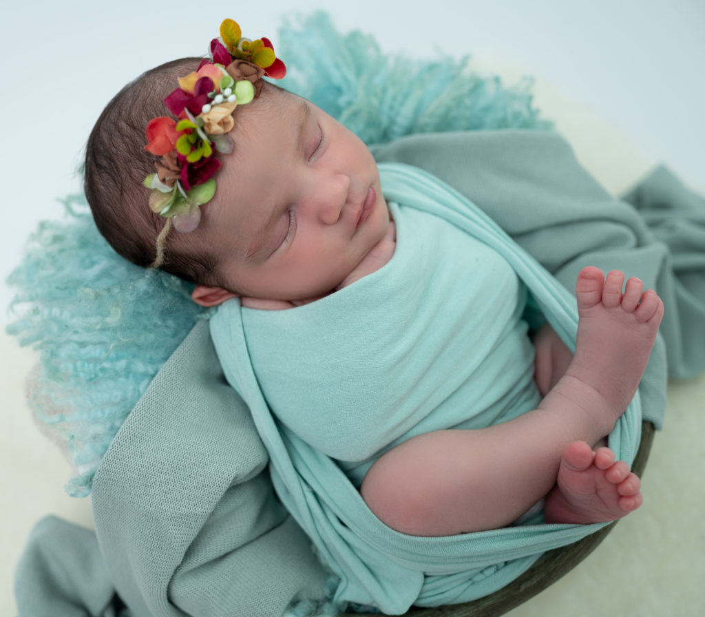 nouvelle-née halo vert et rouge emmaillotée de vert endormie dans une terrine ronde photographe naissance nouveau-né Houilles Yvelines la Défense