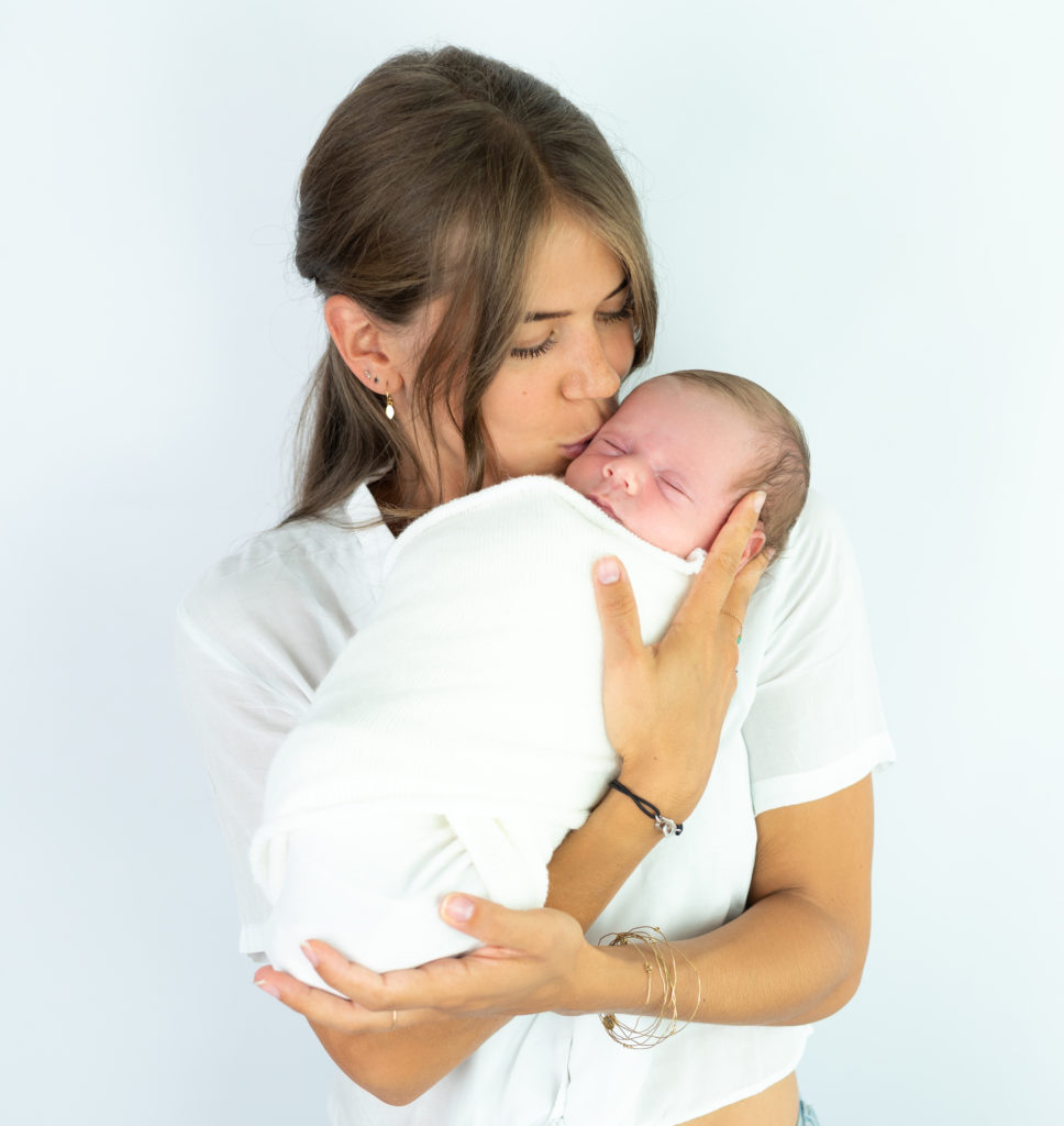 jeune maman embrassant son bébé emmailloté dans ses bras photographe naissance nouveau-né Houilles Yvelines la Défense