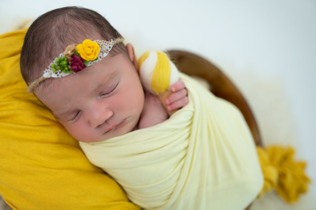 nouvelle-née emmaillotée de jaune pâle endormie dans coeur en bois sur jaune moutarde photographe naissance nouveau-né Houilles Yvelines la Défense