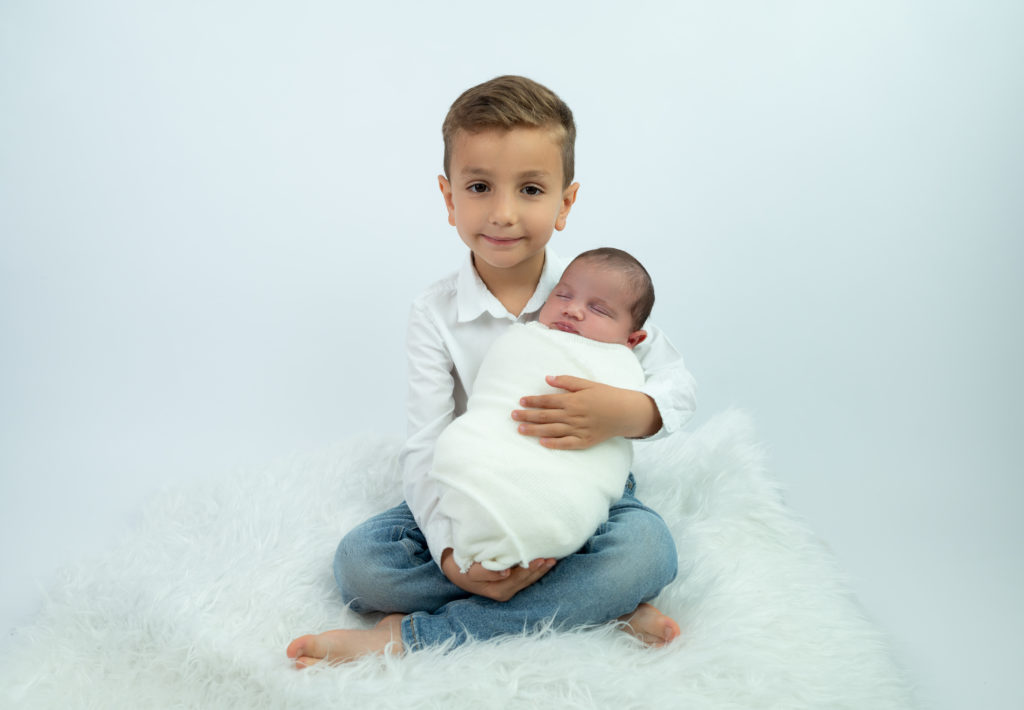 petit garçon tenant sa soeur nouvelle-née dans ses bras photographe naissance bébé famille Houilles Yvelines la Défense