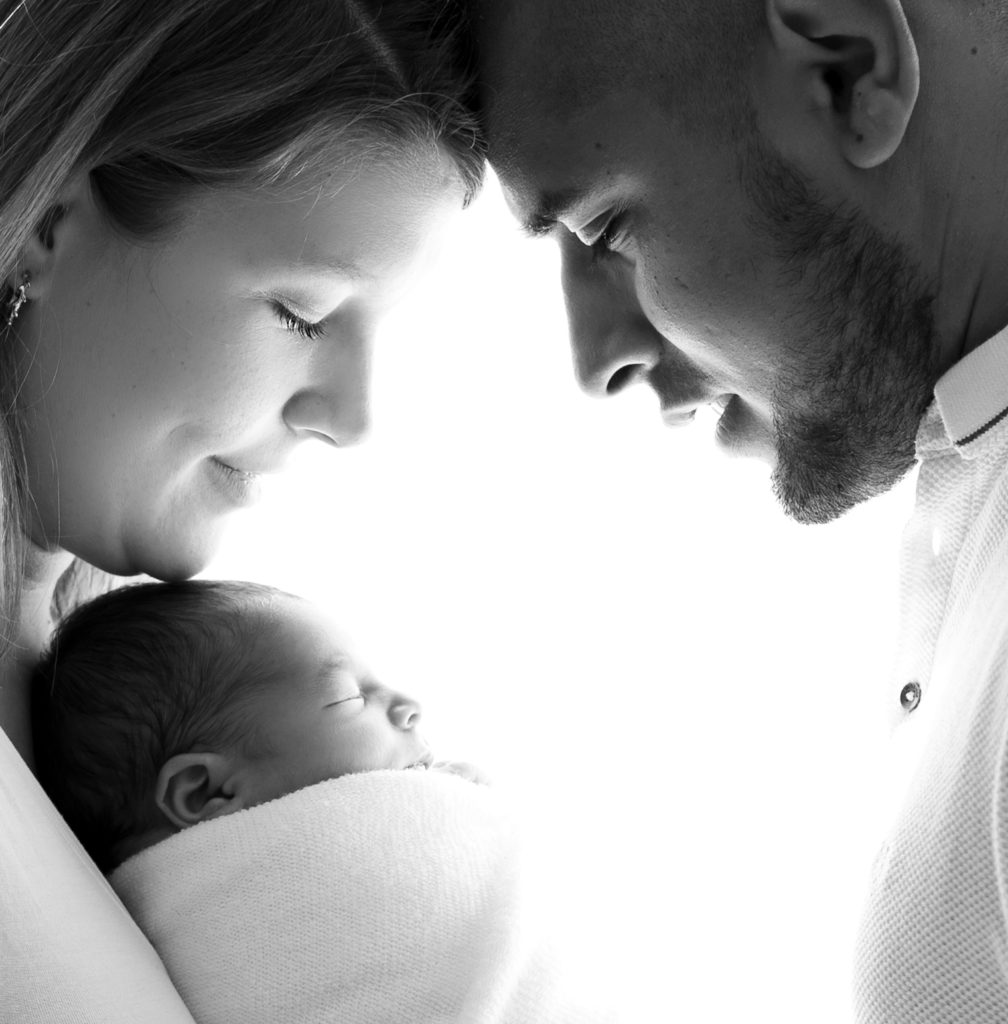 photo noir et blanc contrejour du profil de jeunes parents regardant leur nouveau-né photographe naissance nouveau-né famille Houilles Yvelines la Défense