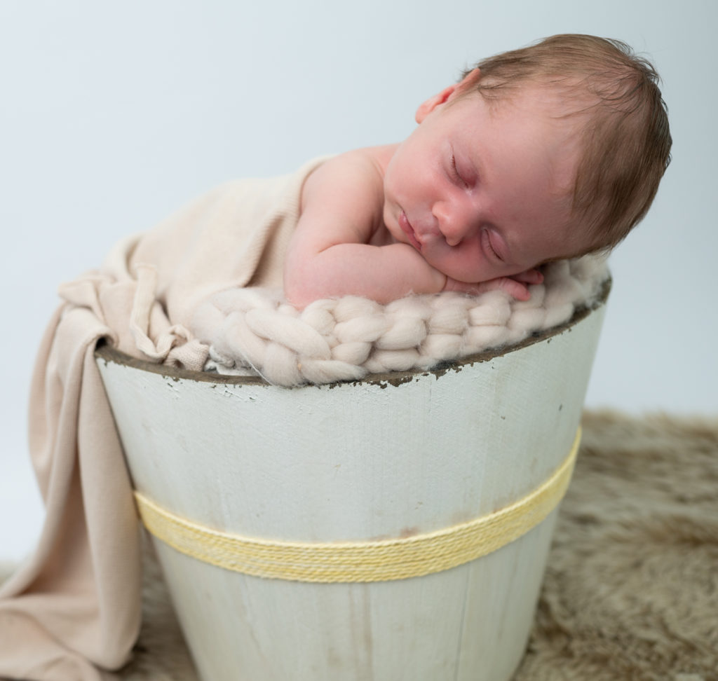 nouveau-né endormi dans un seau en bois dans les tons beige photographe naissance nouveau-né Houilles Yvelines la Défense