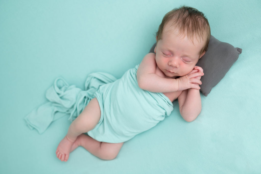 nouveau-né endormi sur posing bag vert menthe sur le côté mains sous la tête et petit oreiller photographe naissance nouveau-né Houilles Yvelines la Défense