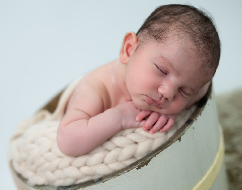 nouveau-né endormi dans un seau en bois tête sur les mains photographe naissance nouveau-né Houilles Yvelines la Défense