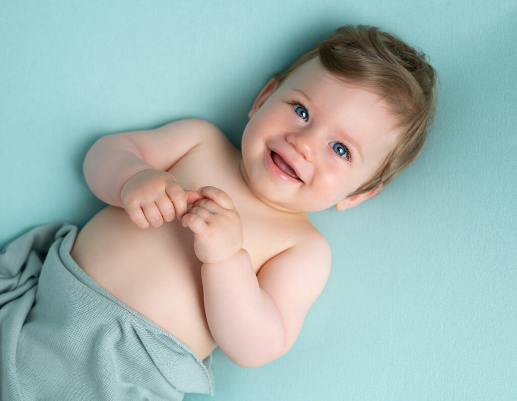 bébé de 10 mois qui sourit allongé sur le dos sur posing bag vert menthe