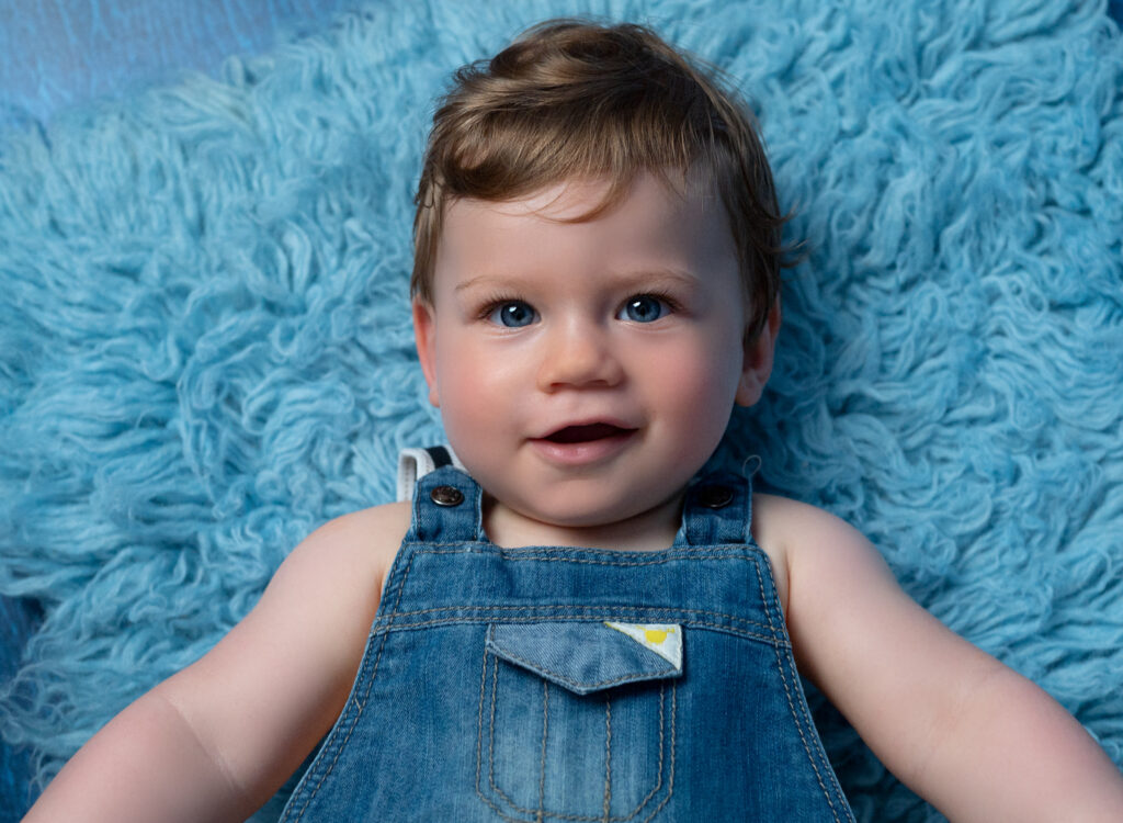bébé de 10 mois qui sourit allongé sur le dos sur flokati bleu