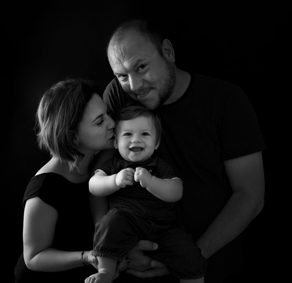 Bébé de 10 mois qui sourit dans les bras de ses parents photographe bébé famille Houilles Yvelines la Défense