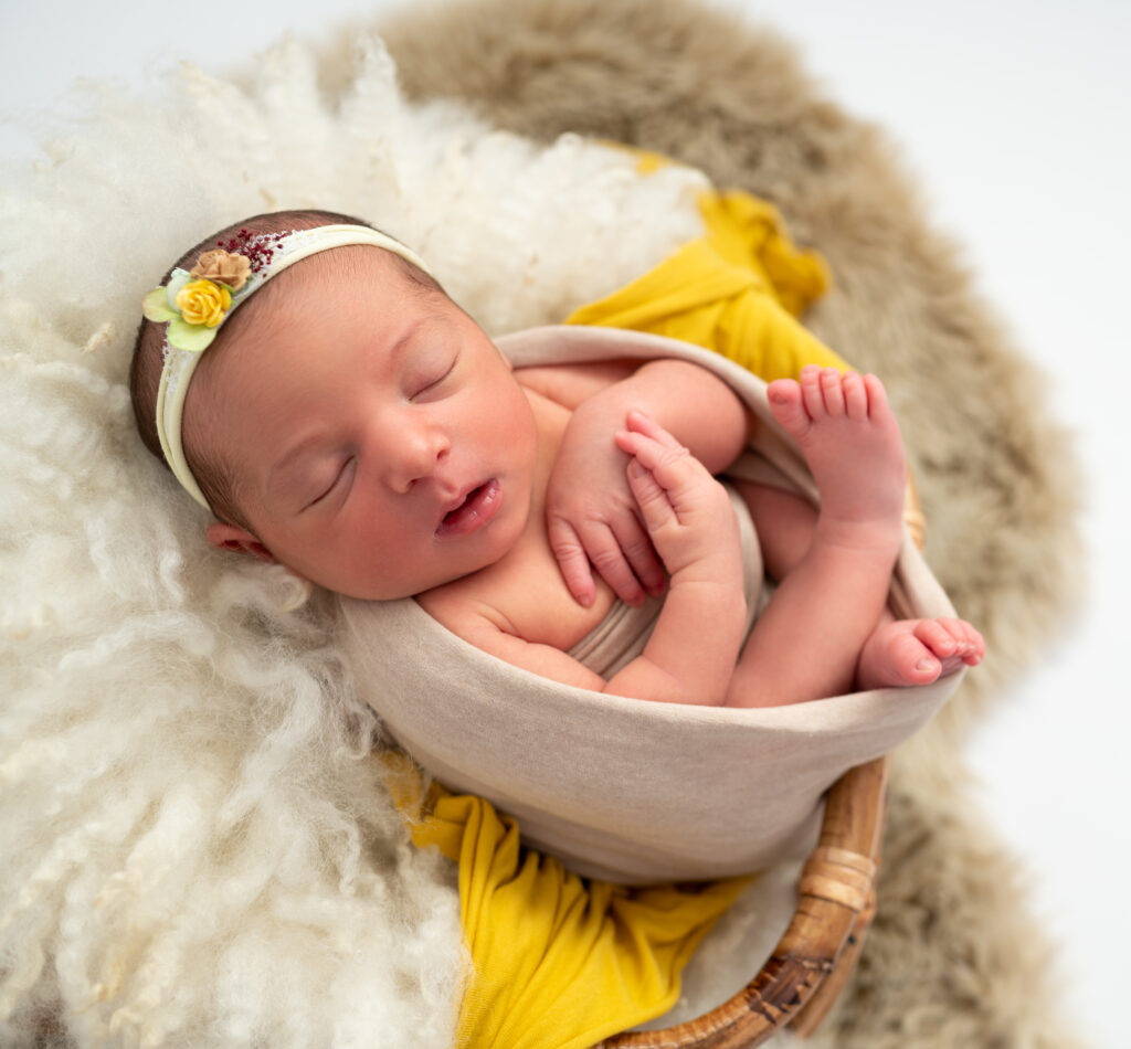 nouvelle-née emmaillotée de jaune pâle dans contenant sur fluffy blanc photographe naissance nouveau-né Houilles Yvelines la Défense