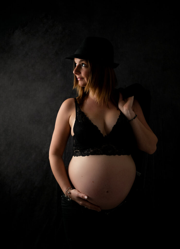 Femme enceinte veste en cuir et chapeau noir sur fond noir photographe grossesse Houilles photographe femme enceinte Houilles photographe grossesse la Défense photographe grossesse Yvelines
