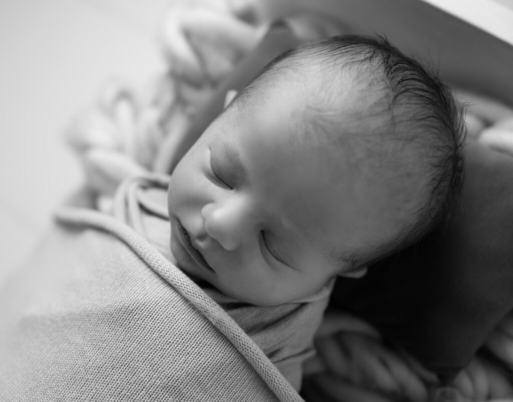 Portrait plan serré d'un nouveau né endormi dans un petit lit photographe naissance houilles photographe naissance la défense photographe naissance yvelines photographe naissance paris