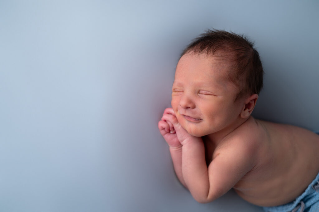 nouveau-né endormi sur fond bleu sourire photographe naissance Houilles photographe naissance la Défense photographe Houilles photographe Versailles photographe Rueil-Malmaison photographe Chatou photographe Yvelines photographe Ile-de-France photographe naissance Yvelines photographe nouveau-né Yvelines photographe bébé Yvelines