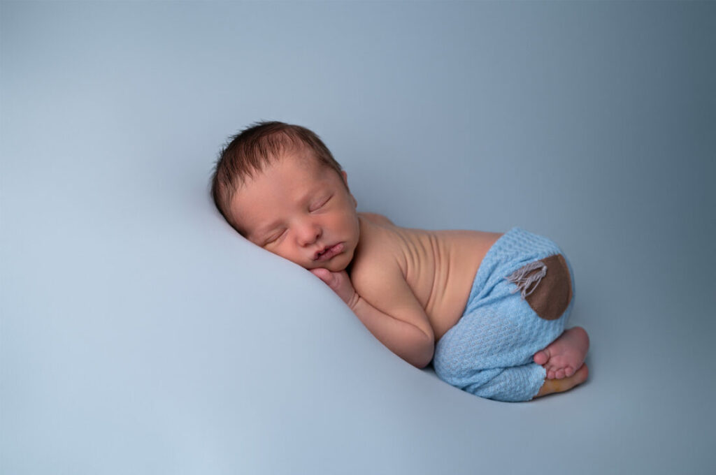 nouveau-né endormi sur fond bleu sourire photographe naissance Houilles photographe naissance la Défense photographe Houilles photographe Versailles photographe Rueil-Malmaison photographe Chatou photographe Yvelines photographe Ile-de-France photographe naissance Yvelines photographe nouveau-né Yvelines photographe bébé Yvelines