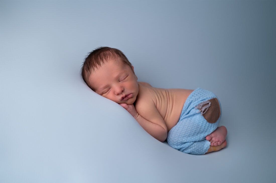 nouveau-né endormi sur fond bleu sourire photographe naissance Houilles photographe naissance la Défense photographe Houilles photographe Versailles photographe Rueil-Malmaison photographe Chatou photographe Yvelines photographe Ile-de-France photographe naissance Yvelines photographe nouveau-né Yvelines photographe bébé Yvelines